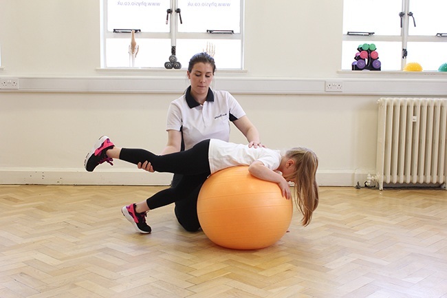 Child lying on therapy ball, therapist providing support