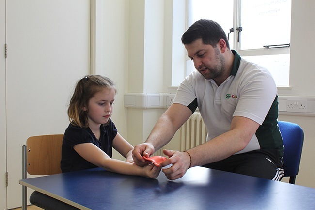 Therapist helping child open her hand against putty