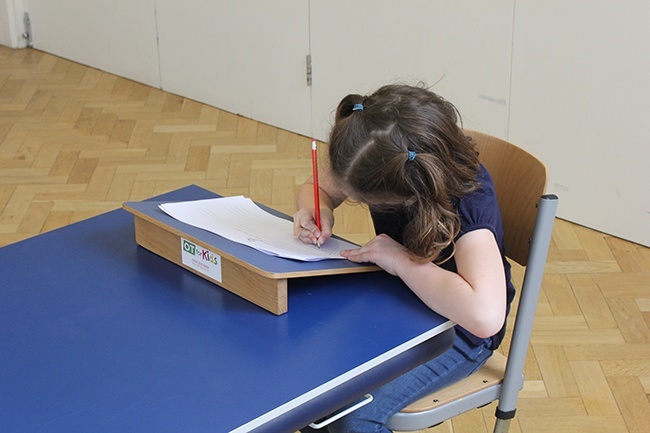 Child writing, using a sloped writing board to help