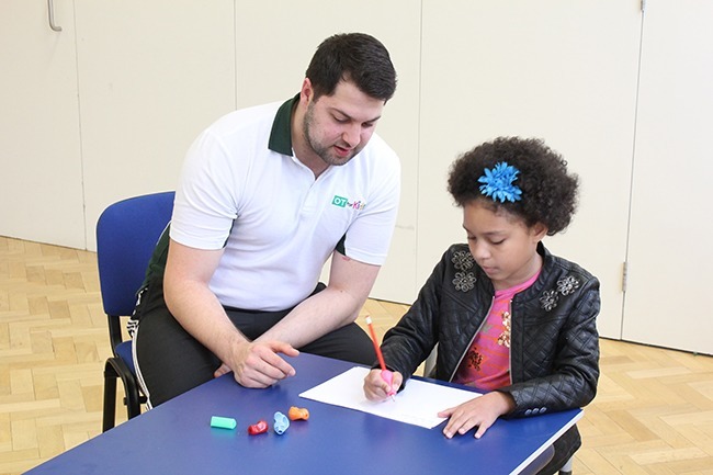 Child writing on assessment, therapist observing