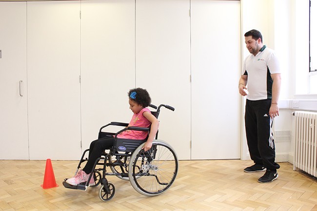 Child sitting in wheelchair, therapist observing