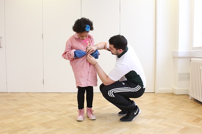 Therapist knelt down helping child do up buttons. Child has gloves on