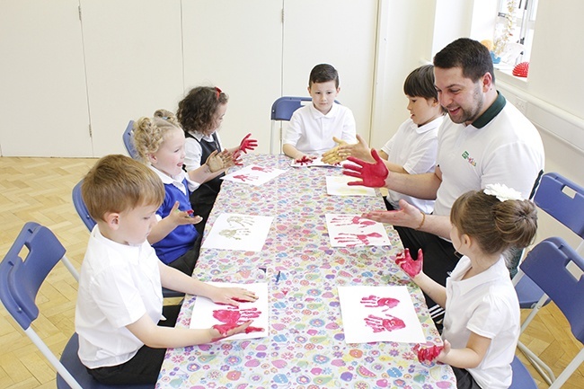 Children with paint on their hands pressing hand prints on paper. Small group, therapist watching 