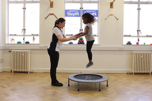 Therapist helping child bounce on a trampoline