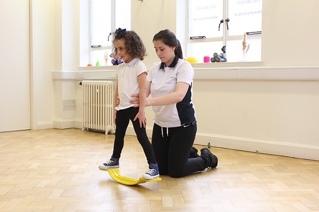 Child balancing on board, therapist providing support at the hips 