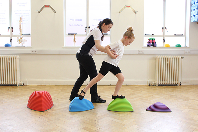 Therapist helping a girl walk across coloured stepping stones