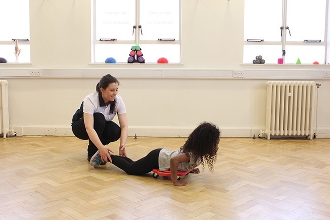 Child lying on scooter board being pulled by therapist